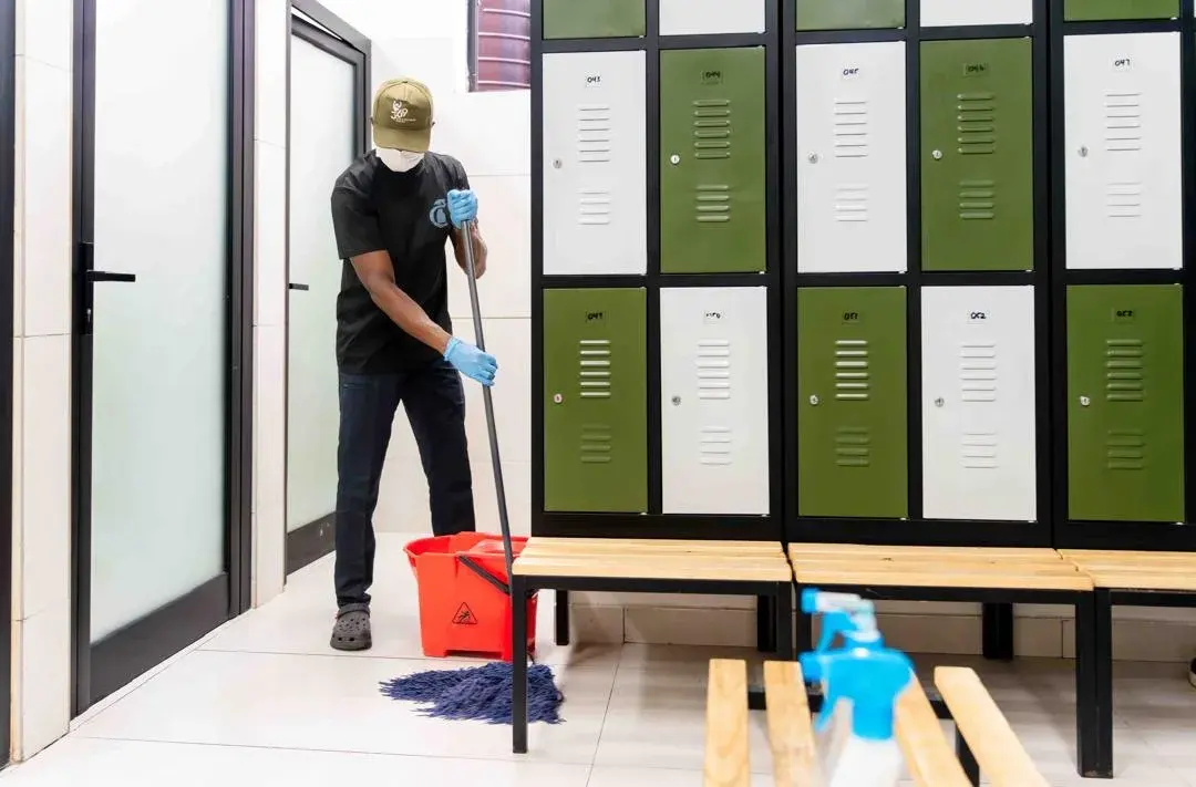 A Clean by AK cleaner mopping a locker room floor between rows of lockers